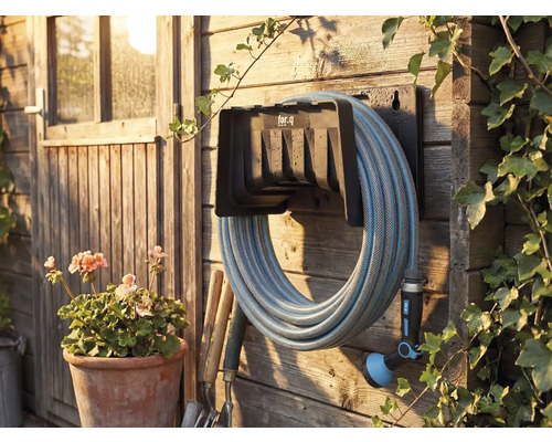 Zahradní scéna s navijákem hadice, namontovaným na dřevěné stěně s zahradní hadicí