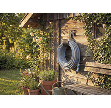 Zahradní scéna s navijákem hadice na dřevěné stěně, obklopená rostlinami