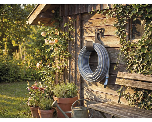 Zahradní scéna s navijákem hadice na dřevěné stěně, obklopená rostlinami