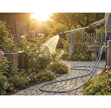 Osoba zavlažuje růže zahradní hadicí na dlážděné cestě.