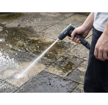 Osoba čistí kamenné desky venku pomocí akumulátorové vysokotlaké myčky.