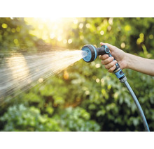 Ruka drží zahradní hadici se sprchovou hlavicí při zavlažování