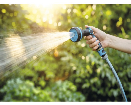 Ruka drží zahradní hadici se sprchovou hlavicí při zavlažování