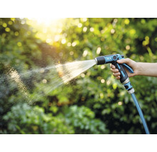 Osoba drží zahradní postřikovač a zalévá rostliny.