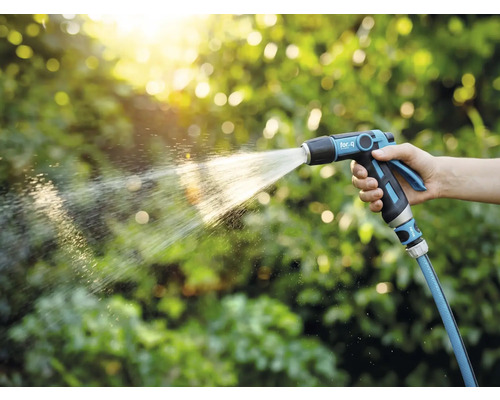 Osoba drží zahradní postřikovač a zalévá rostliny.