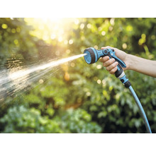 Ruka drží zahradní postřikovač, ze kterého stříká voda