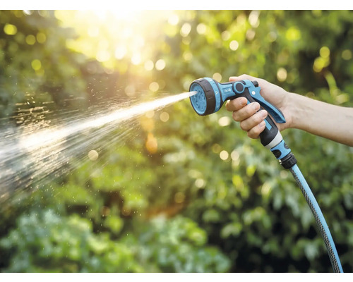 Ruka drží zahradní postřikovač, ze kterého stříká voda