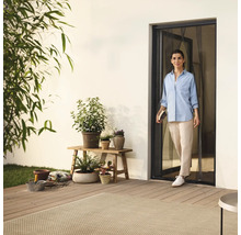 Žena vstupuje na terasu dveřmi se sítí proti hmyzu, obklopena rostlinami a zahradním příslušenstvím.