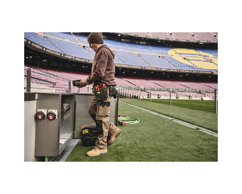 Muž s opaskem na nářadí a pracovním oděvem pracující na elektrické skříni na stadionu.