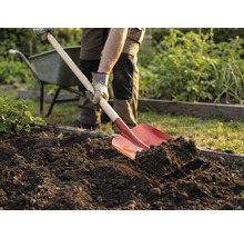 Osoba ryje zeminu v zahradě rýčem. V pozadí je kolečko.