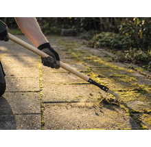 Osoba odstraňuje mech mezi dlažebními kostkami pomocí čističe spár.