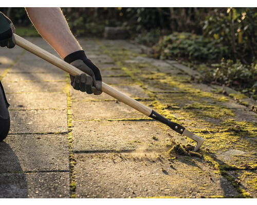 Osoba odstraňuje mech mezi dlažebními kostkami pomocí čističe spár.