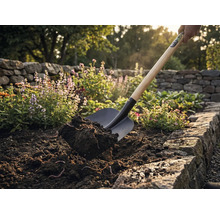 Lopata nabírá zeminu na zahradním záhoně.