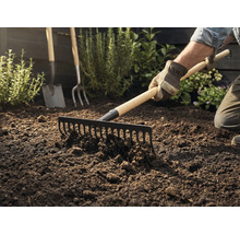 Zahradník hrábě zeminu hráběmi, v pozadí je vidět rýč a vidle.