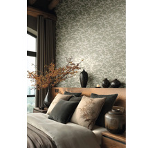 Vliesová tapeta se vzorem borovic v ložnici s dřevěným čelem postele, dekorativními polštáři a keramickými vázami s větvemi.