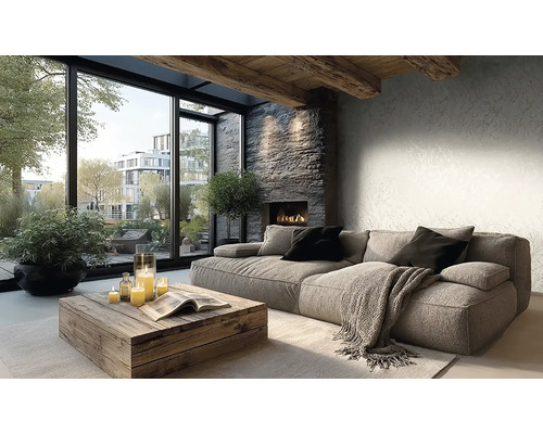 Světlý obývací pokoj s šedou pohovkou, dřevěným stolkem, krbem a velkými okny. Stěna s jemnou tapetou a dřevěné stropní trámy.