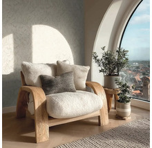 Světlý obývací pokoj s dřevěným křeslem s měkkými polštáři, vzorovanou tapetou a rostlinami před velkým obloukovým oknem.