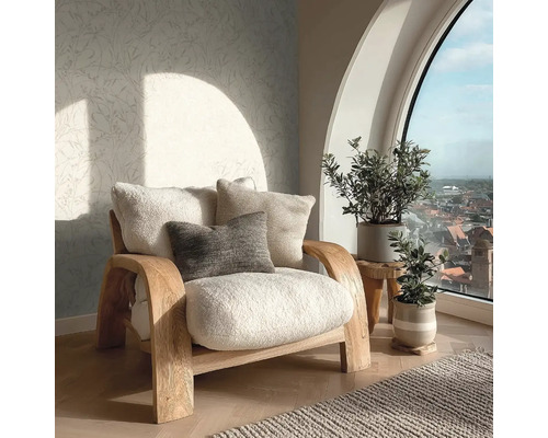 Světlý obývací pokoj s dřevěným křeslem s měkkými polštáři, vzorovanou tapetou a rostlinami před velkým obloukovým oknem.