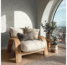 Útulný obývací prostor s dřevěným křeslem, huňatými polštáři, vliesovou tapetou s motivem listů a velkým obloukovým oknem s výhledem na město.