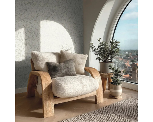 Útulný obývací prostor s dřevěným křeslem, huňatými polštáři, vliesovou tapetou s motivem listů a velkým obloukovým oknem s výhledem na město.