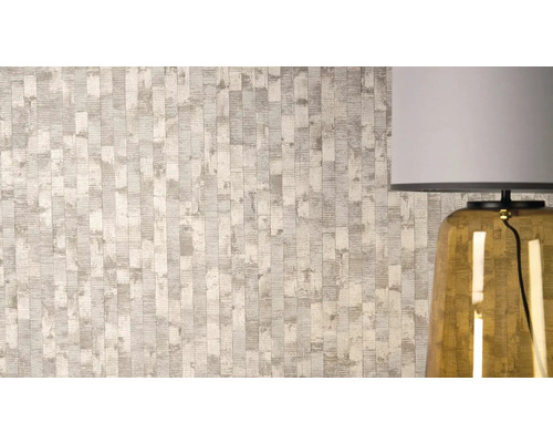 Vliesová tapeta s texturovaným vertikálním vzorem pruhů a metalickými detaily vedle stolní lampy.