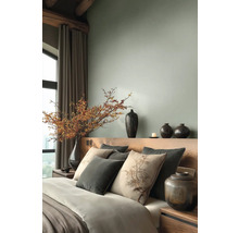 Moderní ložnice s dřevěným čelem postele, dekoračními polštáři a velkou vázou s bobulovými větvemi u okna se závěsy.