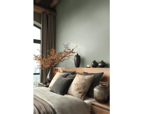 Moderní ložnice s dřevěným čelem postele, dekoračními polštáři a velkou vázou s bobulovými větvemi u okna se závěsy.