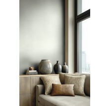 Moderní obývací pokoj se světle šedou stěnou, dřevěnou komodou, dekorativními vázami a pohovkou s látkovými a koženými polštáři u okna.