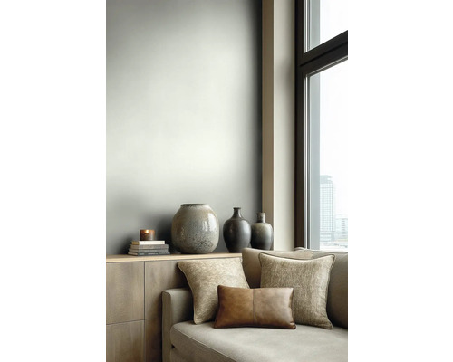 Moderní obývací pokoj se světle šedou stěnou, dřevěnou komodou, dekorativními vázami a pohovkou s látkovými a koženými polštáři u okna.