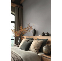 Moderní ložnice s šedou vliesovou tapetou, dřevěným čelem postele, polštáři s motivem stromu a dekorativními tmavými vázami.