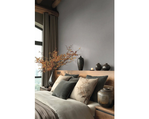 Moderní ložnice s šedou vliesovou tapetou, dřevěným čelem postele, polštáři s motivem stromu a dekorativními tmavými vázami.