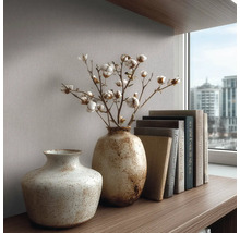 Strukturované keramické vázy s bavlněnými větvičkami a knihami na dřevěné polici před tapetou u okna.