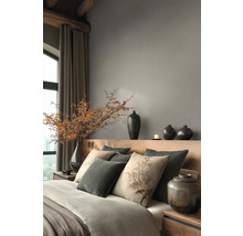 Moderní ložnice s dřevěným čelem postele, šedými stěnami, dekoračními polštáři, keramickými vázami a velkou větví s bobulemi ve váze.