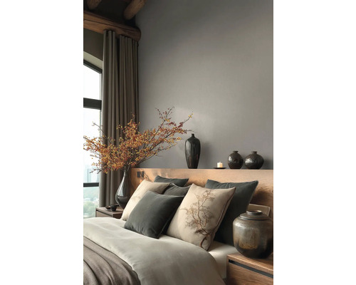 Moderní ložnice s dřevěným čelem postele, šedými stěnami, dekoračními polštáři, keramickými vázami a velkou větví s bobulemi ve váze.