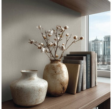 Dvě strukturované keramické vázy na dřevěné polici, jedna s bavlníkem, vedle stohu knih před strukturovanou stěnou.