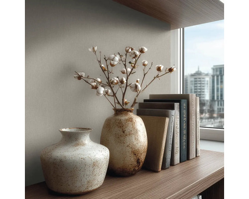 Dvě strukturované keramické vázy na dřevěné polici, jedna s bavlníkem, vedle stohu knih před strukturovanou stěnou.