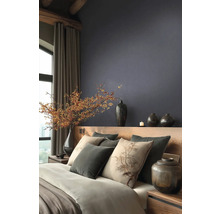 Moderní ložnice s tmavou strukturovanou tapetou, dřevěnou postelí, polštáři s motivem stromu a dekorativními vázami s větvemi bobulí.