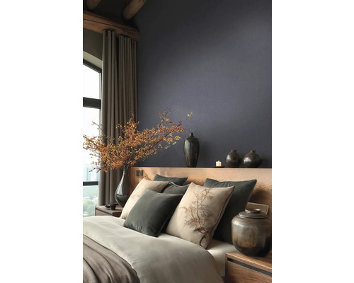 Moderní ložnice s tmavou strukturovanou tapetou, dřevěnou postelí, polštáři s motivem stromu a dekorativními vázami s větvemi bobulí.