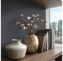 Strukturovaná tapeta v tmavě modré barvě za dvěma keramickými vázami s bavlníkovými větvemi a knihami na dřevěné polici v moderním stylu.