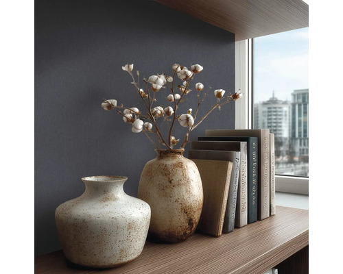 Strukturovaná tapeta v tmavě modré barvě za dvěma keramickými vázami s bavlníkovými větvemi a knihami na dřevěné polici v moderním stylu.