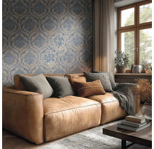 Světlý obývací pokoj s modro-béžovou damaškovou tapetou za hnědou koženou pohovkou s polštáři a dřevěným oknem.