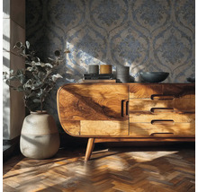 Obývací pokoj s tapetou s ornamenty, komodou z masivního dřeva, vázou s rostlinou a parketami se stromečkovým vzorem.