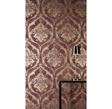 Vliesová tapeta s barokním damaškovým vzorem ve zlaté barvě na červeném podkladu, se zlatou stolní lampou na tmavém stole.