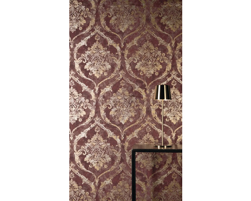 Vliesová tapeta s barokním damaškovým vzorem ve zlaté barvě na červeném podkladu, se zlatou stolní lampou na tmavém stole.