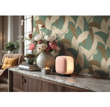 Moderní pokoj s tapetou s velkými listy. Na komodě s mramorovou deskou stojí stolní lampa, váza s květinami a dekorace.