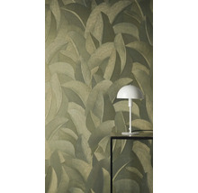 Vliesová tapeta se strukturovaným vzorem tropických listů. Bílá stolní lampa na černém stolku stojí před stěnou.