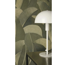 Vliesová tapeta s velkým motivem palmových listů v zelených odstínech za bílou stolní lampou na tmavém stole.