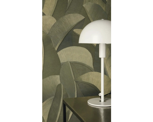 Vliesová tapeta s velkým motivem palmových listů v zelených odstínech za bílou stolní lampou na tmavém stole.