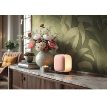 Moderní stolní lampa ve tvaru kvádru s měkkým světlem na komodě s mramorovou deskou, kytice ve váze a tapeta s listovým vzorem.