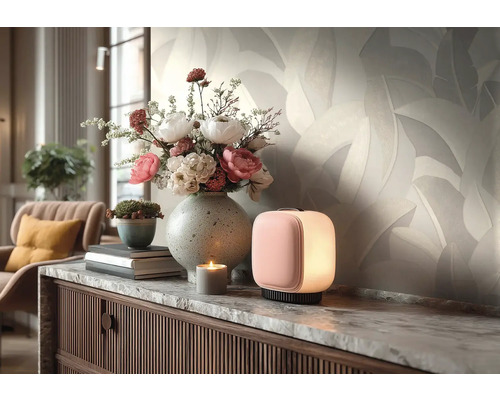 Světlá vliesová tapeta s motivem listů v obývacím pokoji za komodou s vázou s květinami a malou lampou.